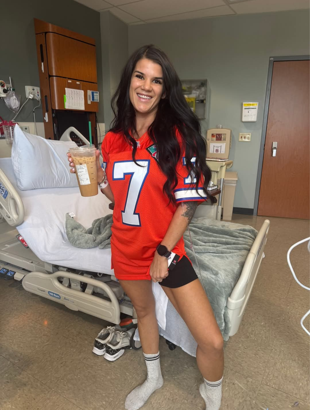 Kari smiling in her hospital room holding an iced coffee